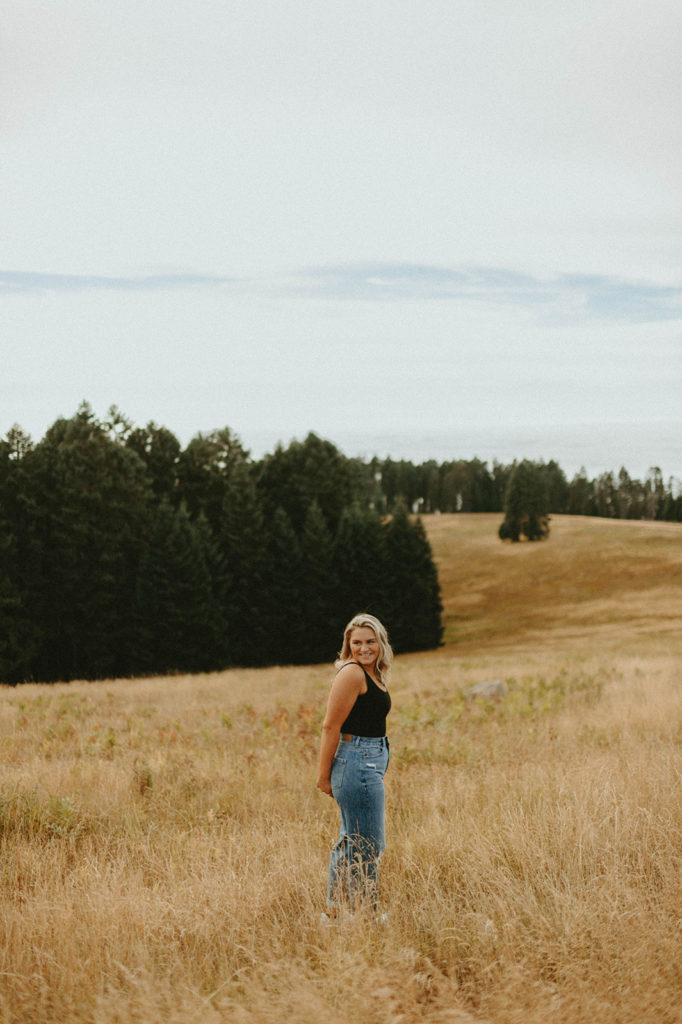 Senior standing on hillside in black tank top and jeans