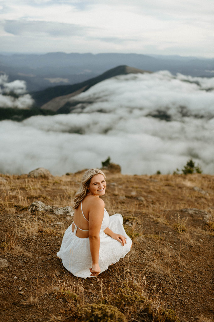 senior sitting on hillside with clouds in the background