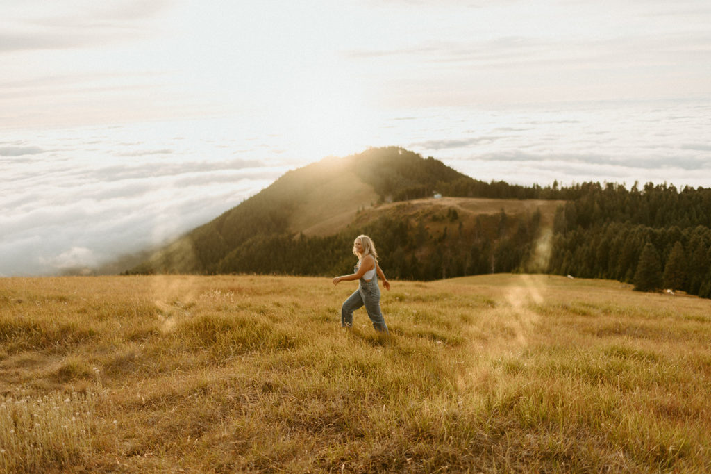 girl in white shirt and overalls walking through grassy hills in Mary's Peak, Oregon