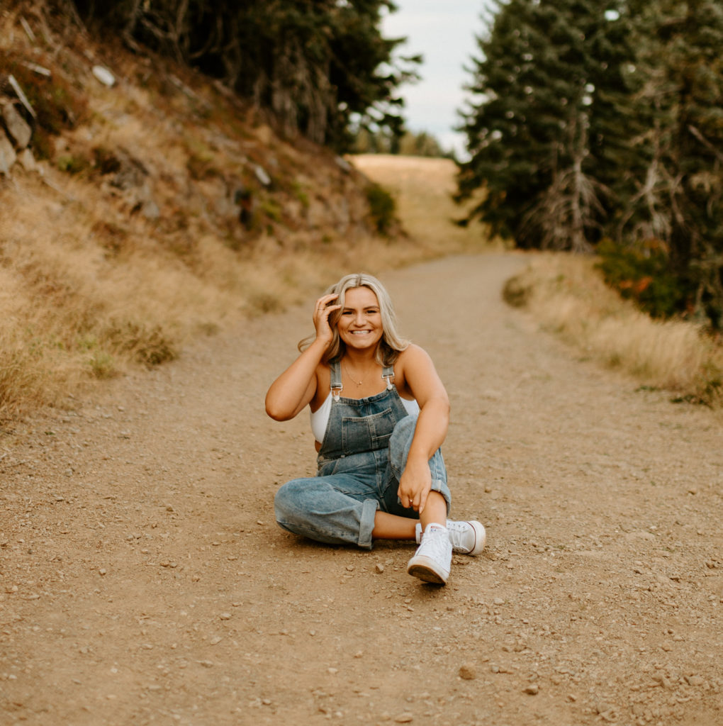 senior sitting on dirt path in overalls