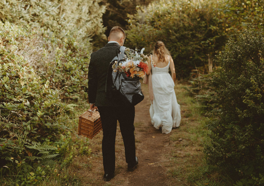 Groom hiking with backpack and flowers at elopement