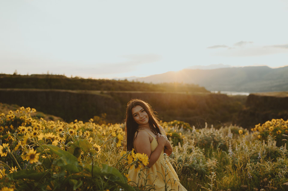 Young woman looking back over her shoulder in a field of yellow flowers during sunset