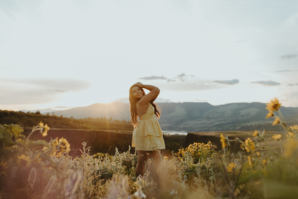 Woman holding her head and smiling in a sunlit field with distant mountains