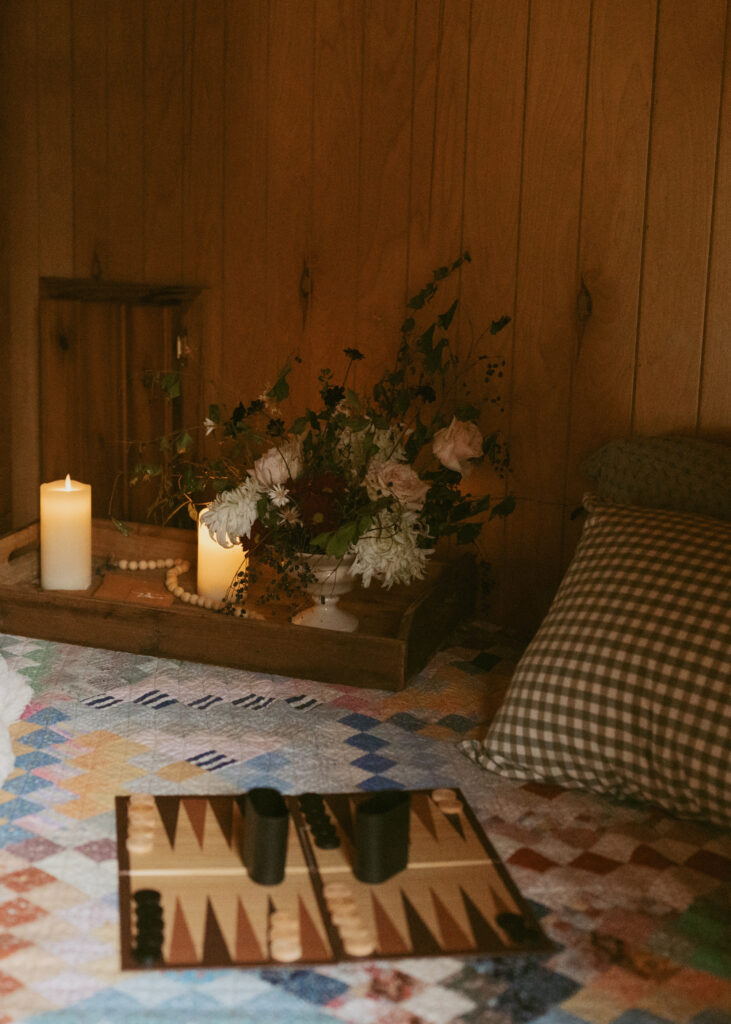 Cozy indoor setting with a quilt-covered bed, a tray with flowers and candles, and a backgammon board ready for play