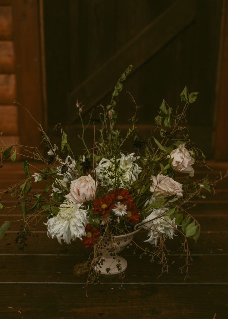 A rustic floral arrangement in a vintage vase, set against a dark wooden floor