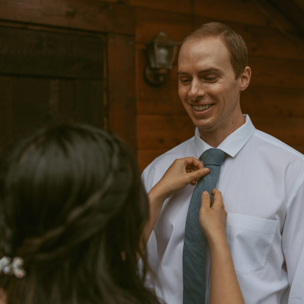 Groom happily looking at his bride while bride is fixing his tie