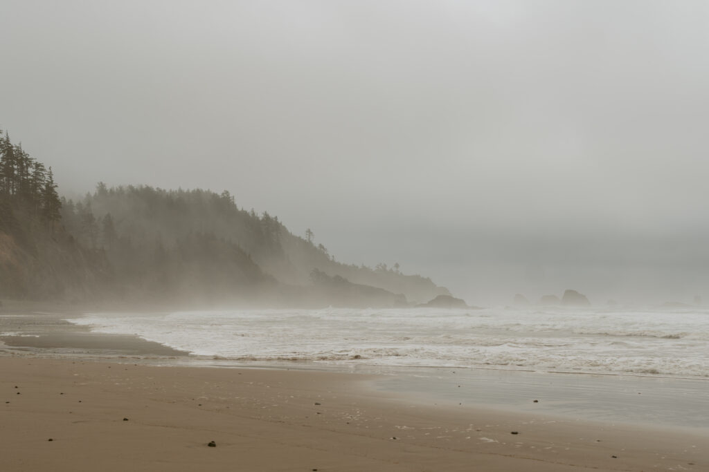 Serene Cannon Beach with waves crashing on the sandy shore and fog-shrouded cliffs in the background