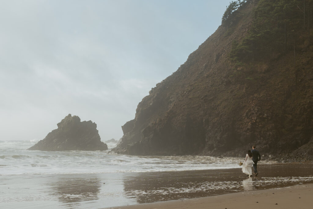 Bride and groom holding each other walking on the sand to the seashore