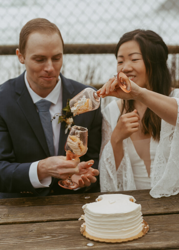 Groom holds his glass with the cake inside and bride turning the glass upside down 