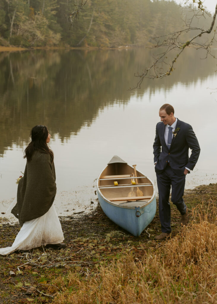 Bride wearing a jacket and groom on his wedding suit about to ride a canoe