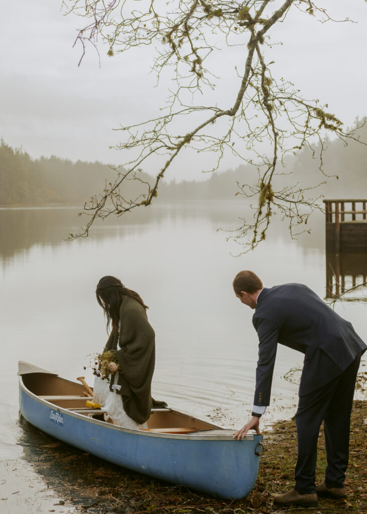 Bride in her jacket riding the canoe and groom holding it