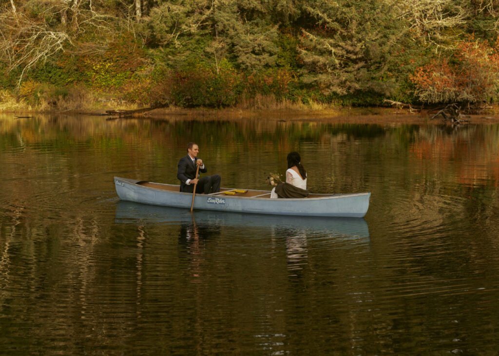 Newlywed couple sitting across each other, and the groom paddling across the serene lake for their dreamy elopement