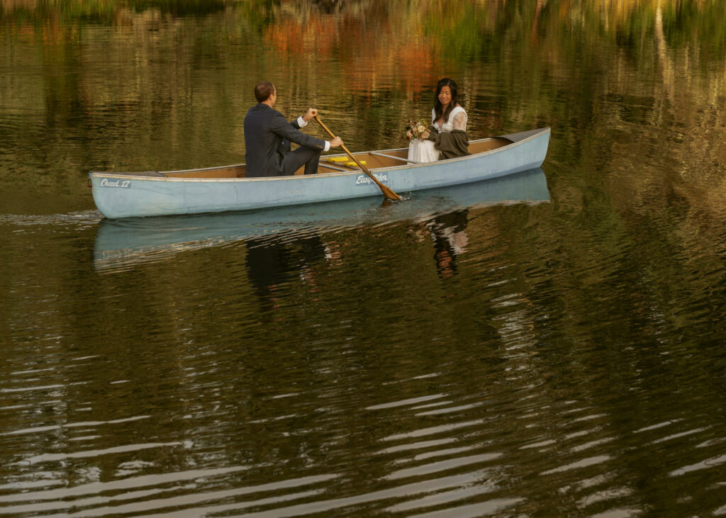Bride and groom couple sitting across each other, and the groom paddling across the lake for their dreamy elopement