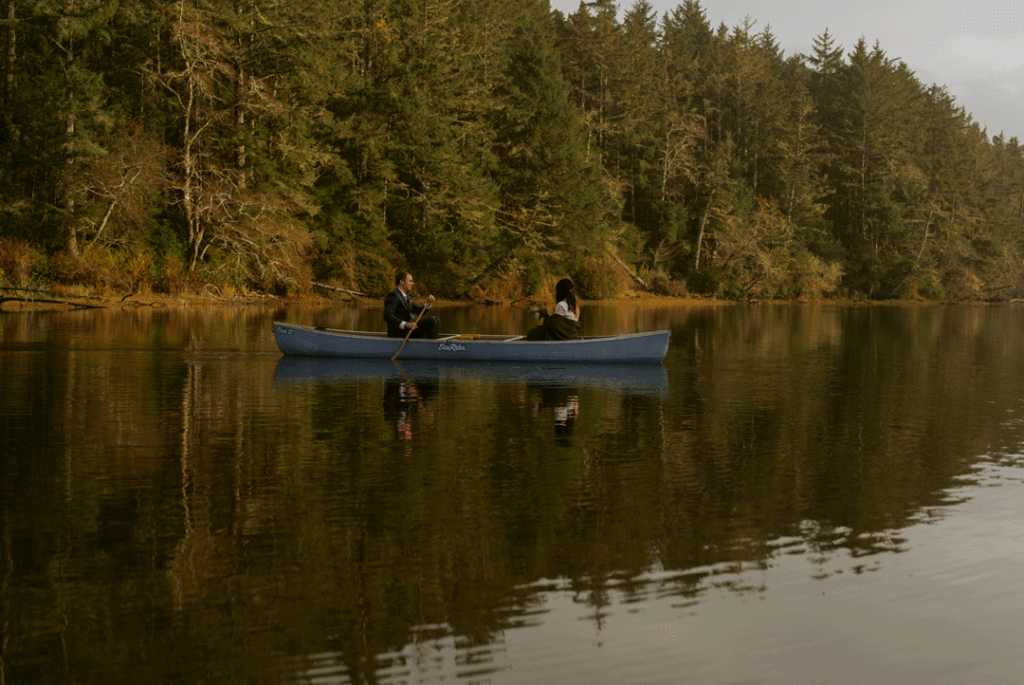 Newlywed couple sitting across each other, and the groom paddling across the serene lake for their dreamy elopement