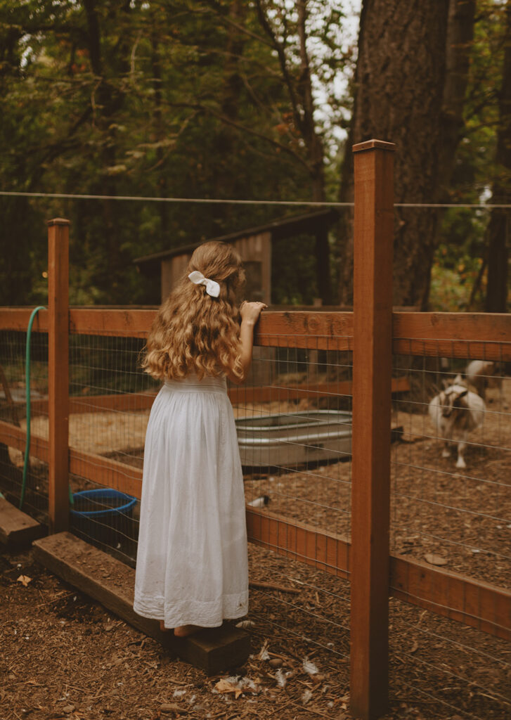 Young woman wearing her white dress looking to the animal in a farmyard