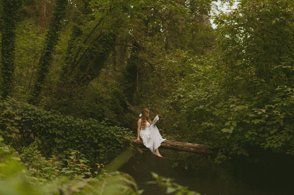 Serene scene of a young woman in a white dress sitting on a log in above the river 