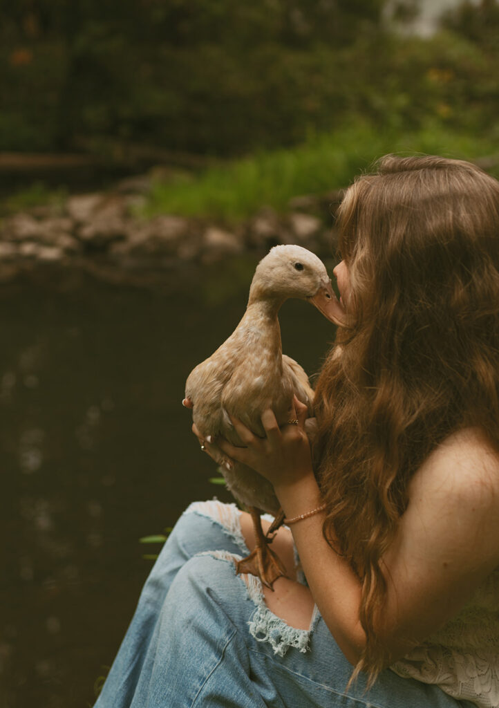 young woman holding a duck by a pond for her cottage core aesthetic photo session in Oregon