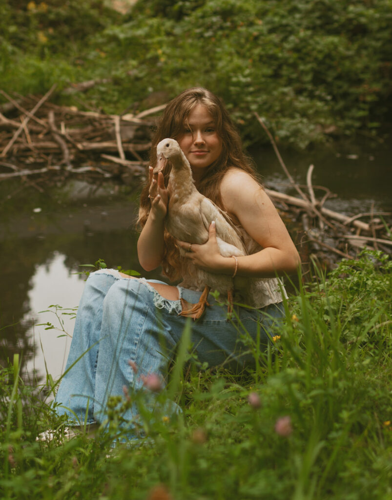 young woman holding a duck by a pond for her cottage core aesthetic photo session in Oregon