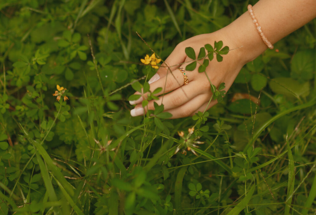Close up photo of the young woman's hand wearing her gold ring about to pick a yellow flower
