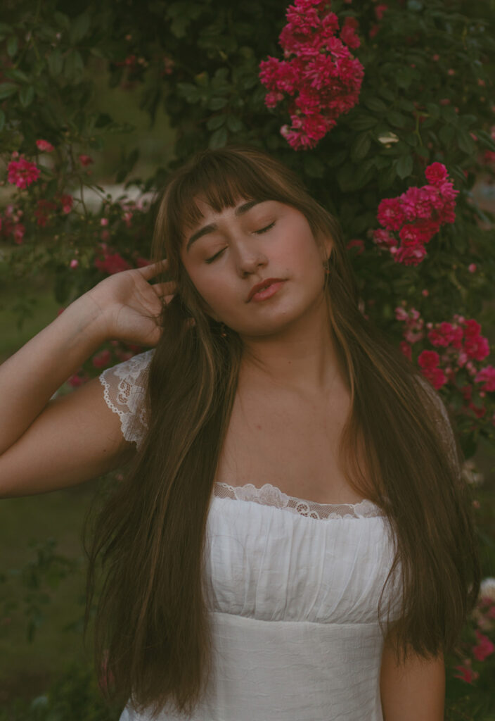 Young woman in her beautiful white dress, closed eyes and leaning her back to the pink flowers