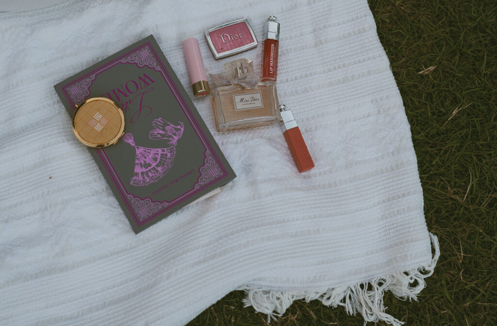 Beauty products and a book laid out on a white blanket on grass