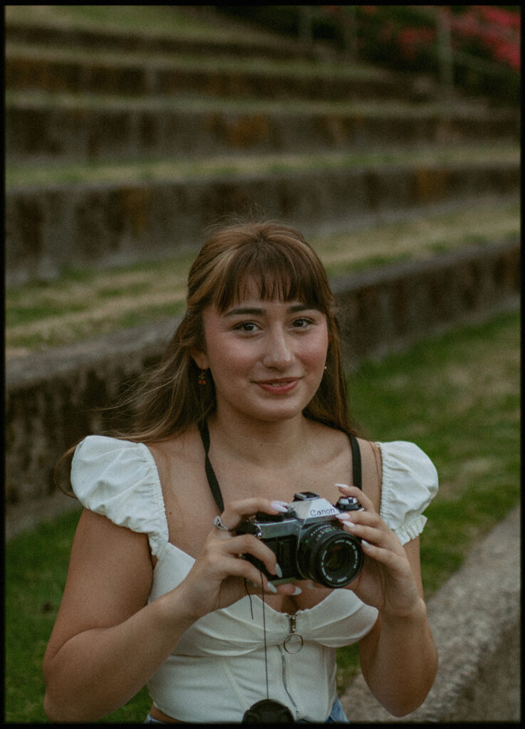 young woman holding a camera, standing on stone steps
