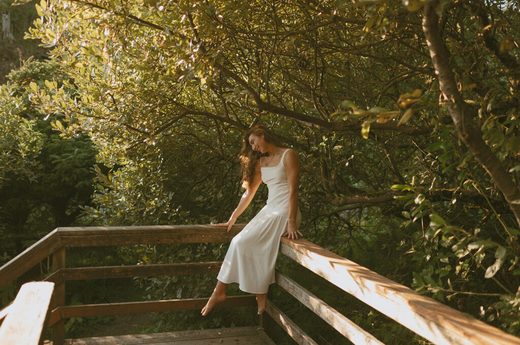girl in white dress sitting on railing in a forest in Oregon