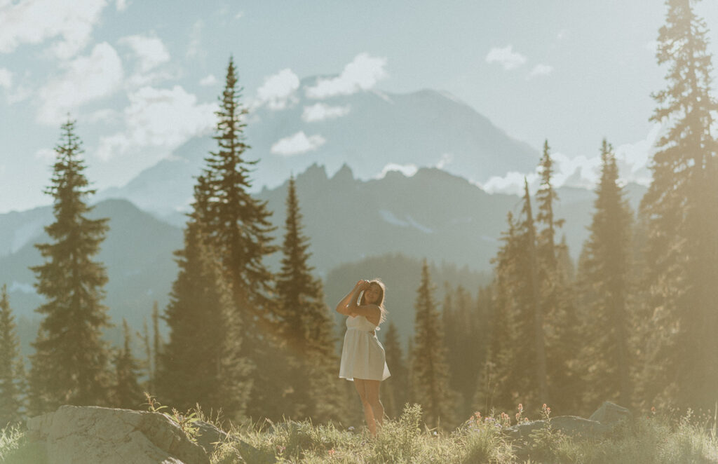 girl in white dress standing in the forest in front of mountains
