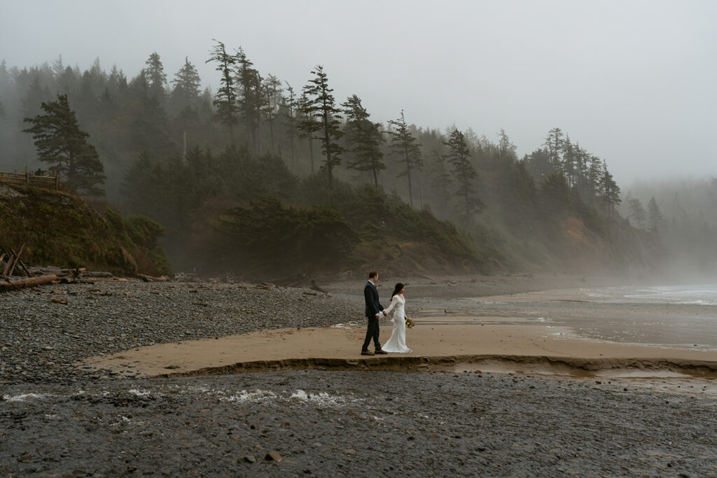 bride and groom walking along beach together in misty weather at Ecola State Park