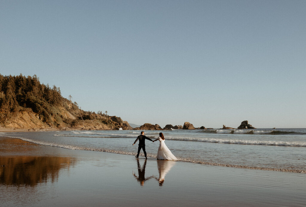 Bride and groom walking along beach at Ecola State Park in Oregon