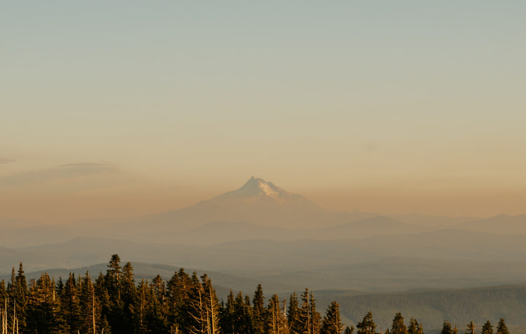 Distant view of a mountain peak at sunset, with a hazy orange sky and forest silhouette