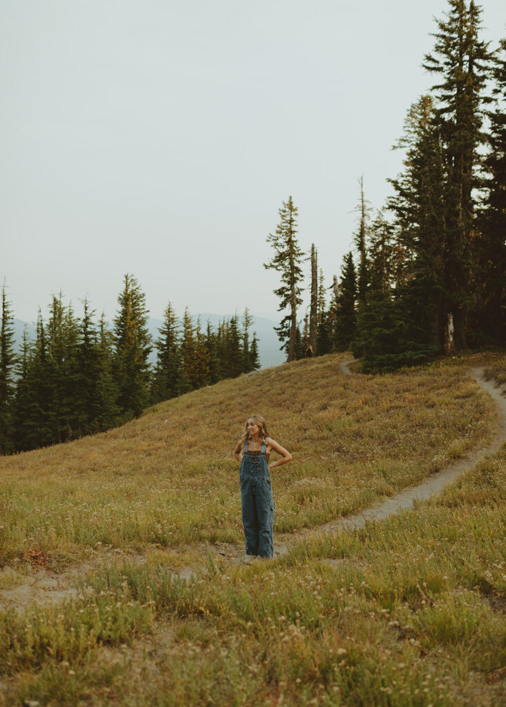 Woman walking alone on a mountain trail surrounded by tall pine trees for her senior session in Oregon