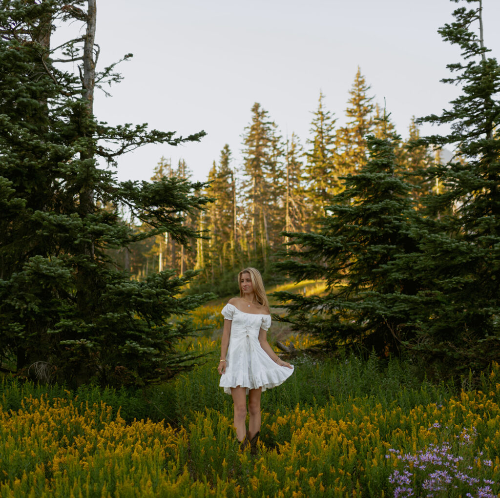 girl in white dress standing in grassy area next to mountain range