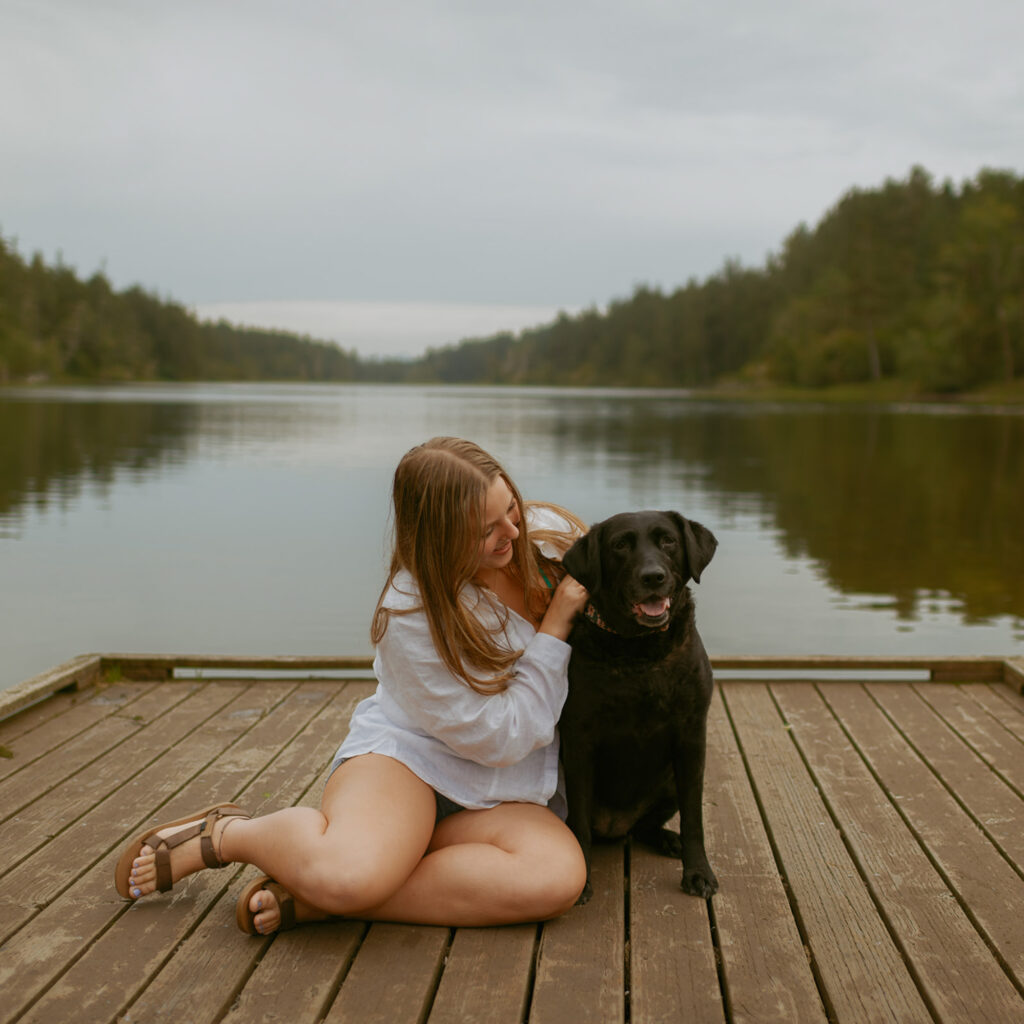 girl on a dock sitting with her black labrador