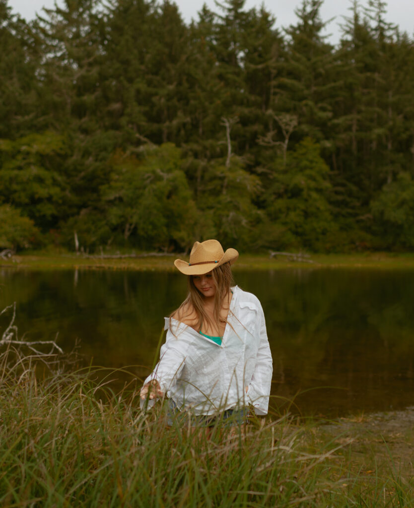 girl in white shirt walking through tall grass alongside a lake on the Oregon coast