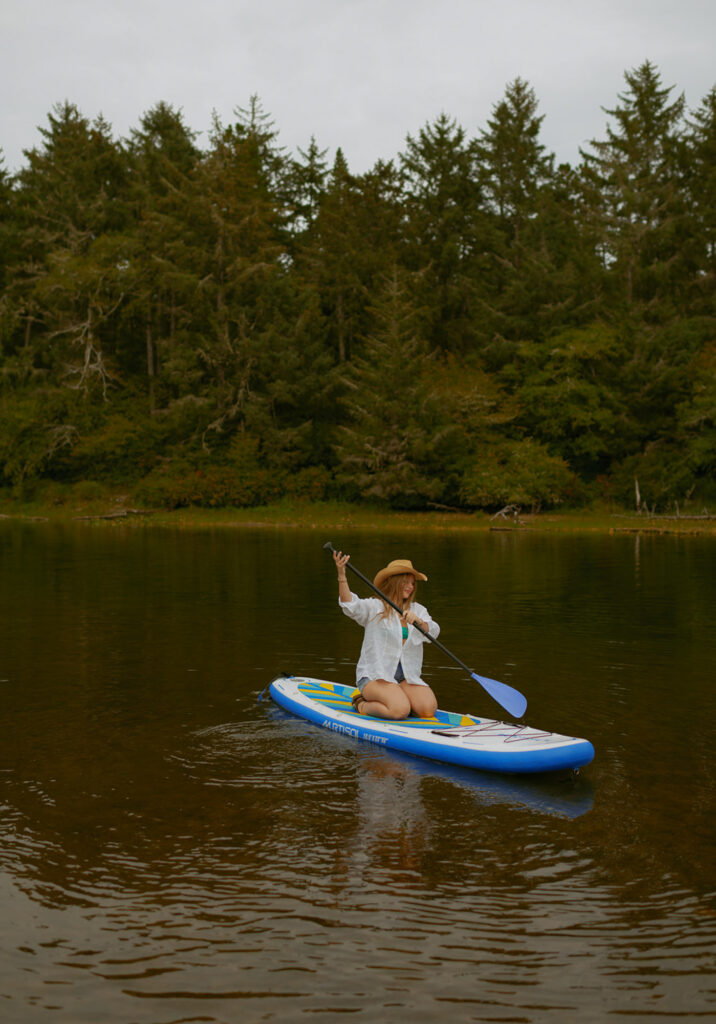 girl in white shirt and cowgirl hat paddle boarding on a lake at the Oregon coast