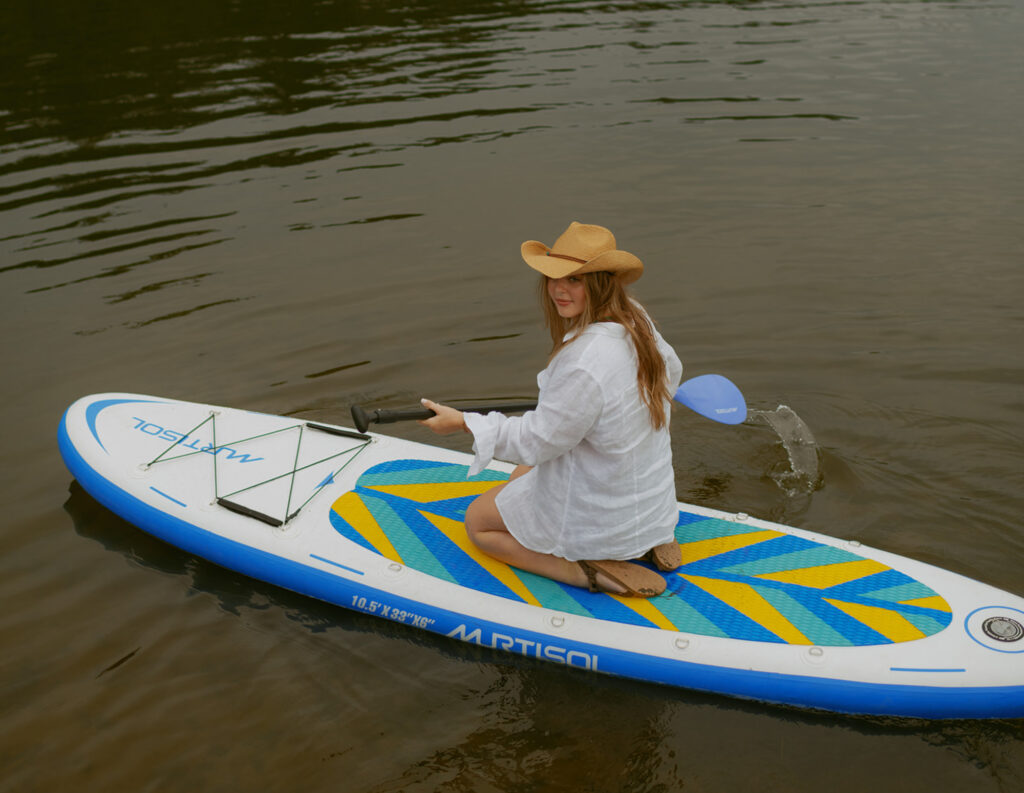 girl in white shirt and cowgirl hat paddle boarding on a lake at the Oregon coast