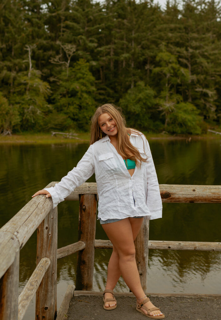 girl standing next to lake in white button up shirt over a swimsuite