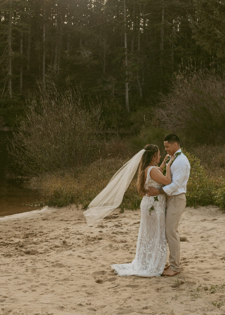 bride and groom standing in a sandy shore, embracing each other