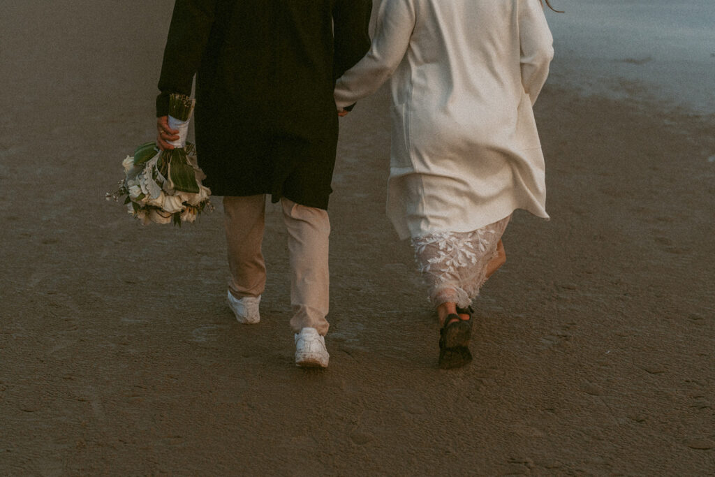 bride and groom walking away on a sandy beach, holding hands