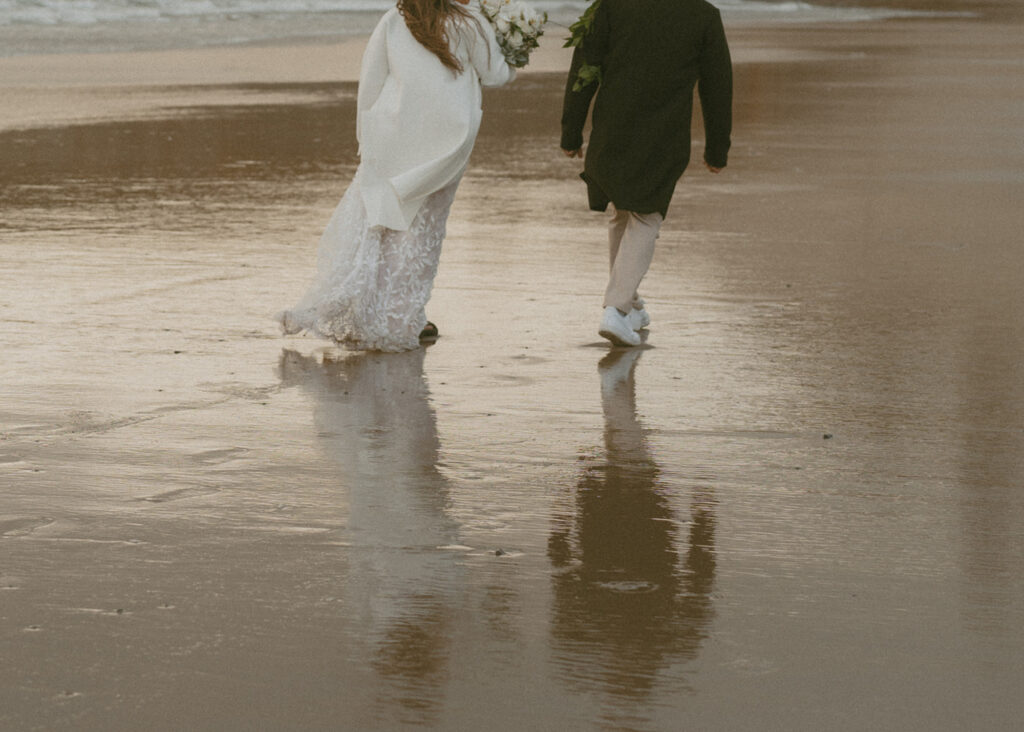 couple walking away on a wet, sandy beach towards the ocean