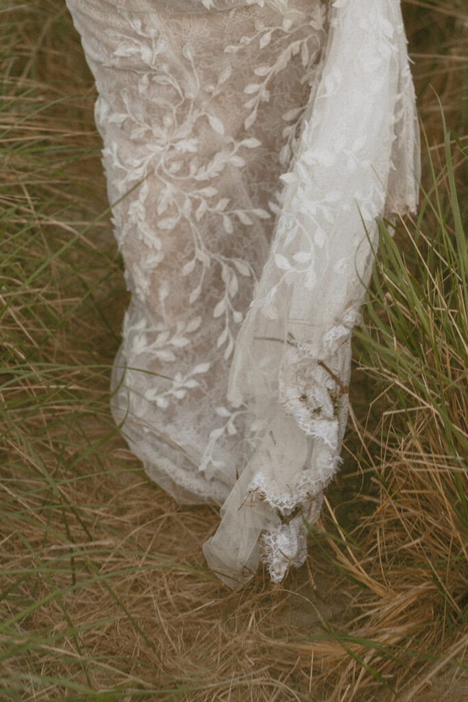 Close-up of a white, embroidered lace dress draping over dry grass