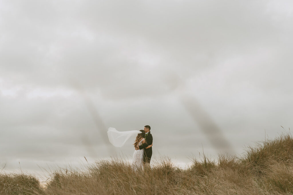 bride and groom standing on a grassy hill