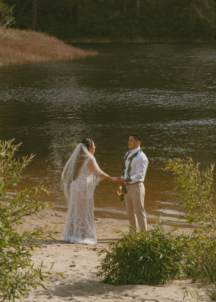 couple standing at the edge of a tranquil body of water, holding hands and facing each other