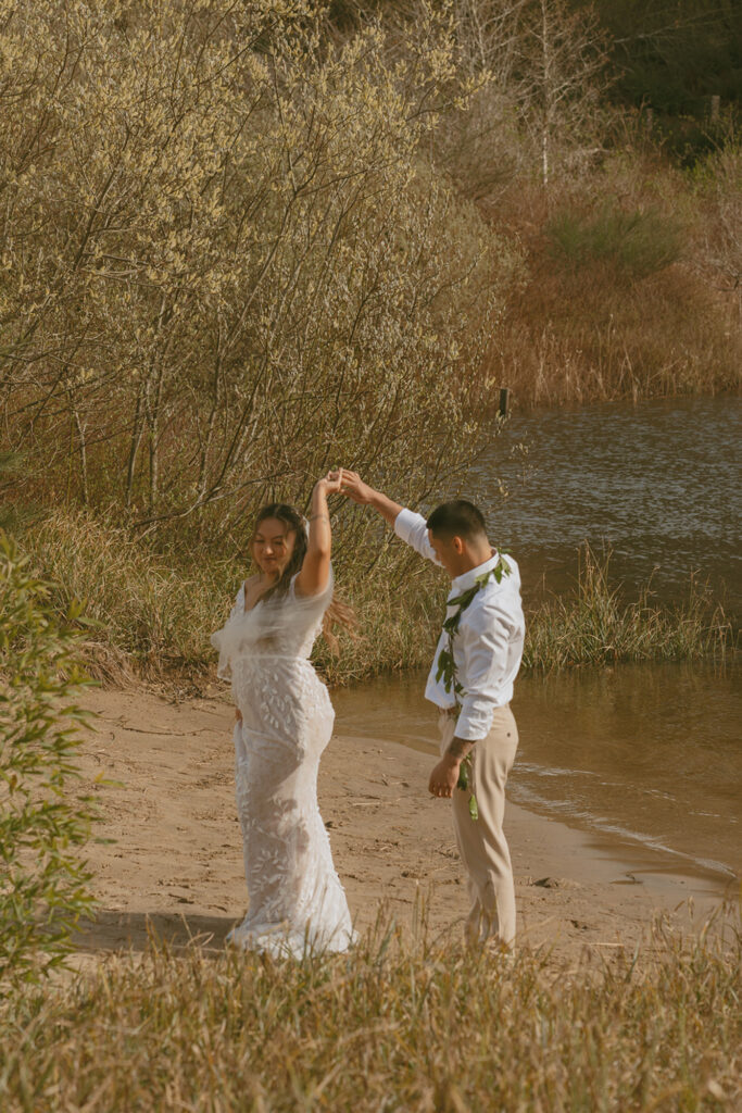 groom twirling a bride around on a sandy beach near the river