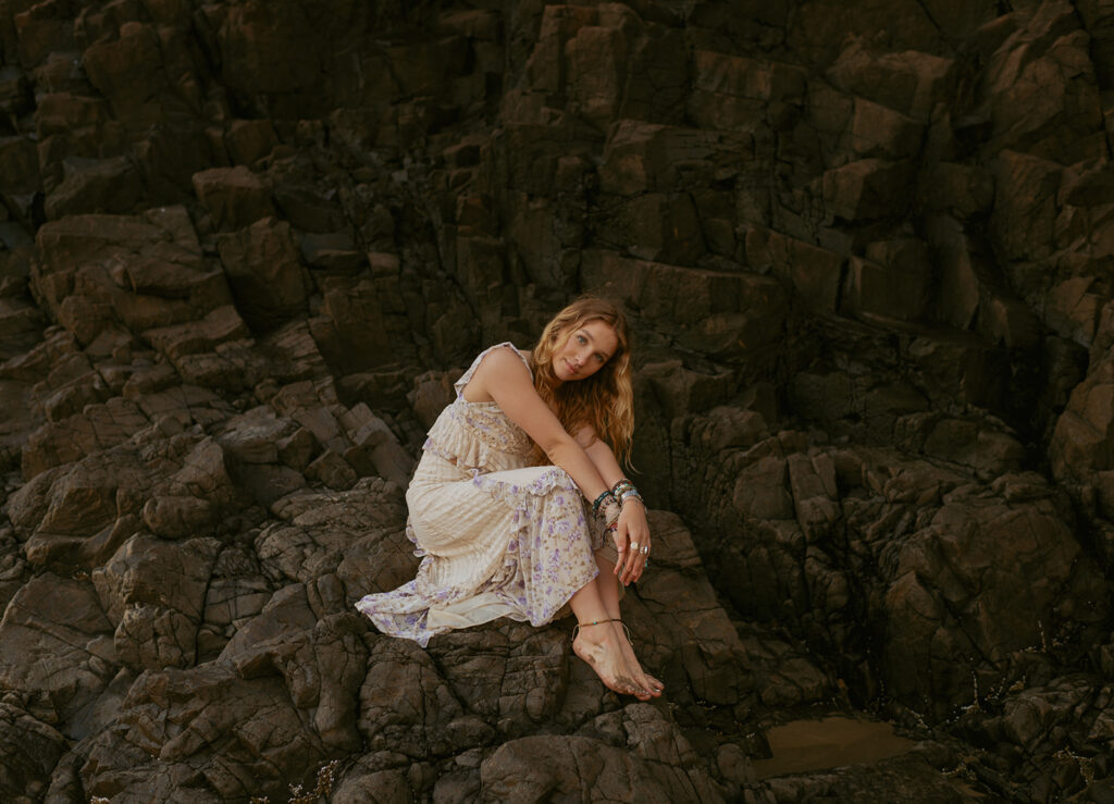 girl wearing white dress sitting on rocks at the beach