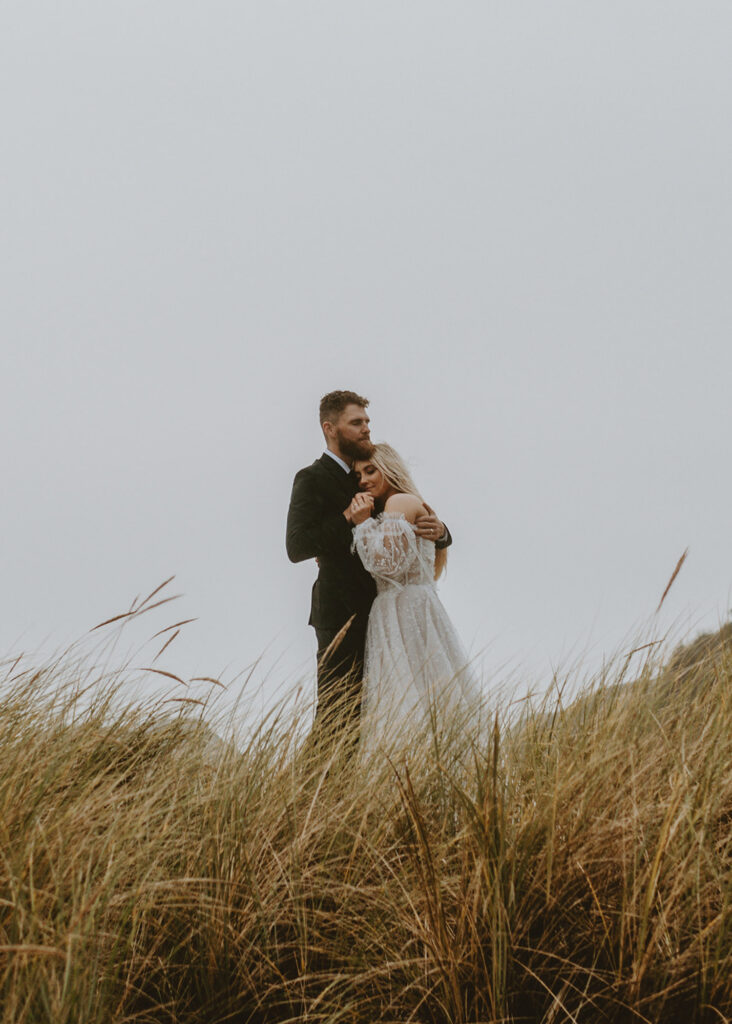 bride and groom hugging each other in a field of tall grass