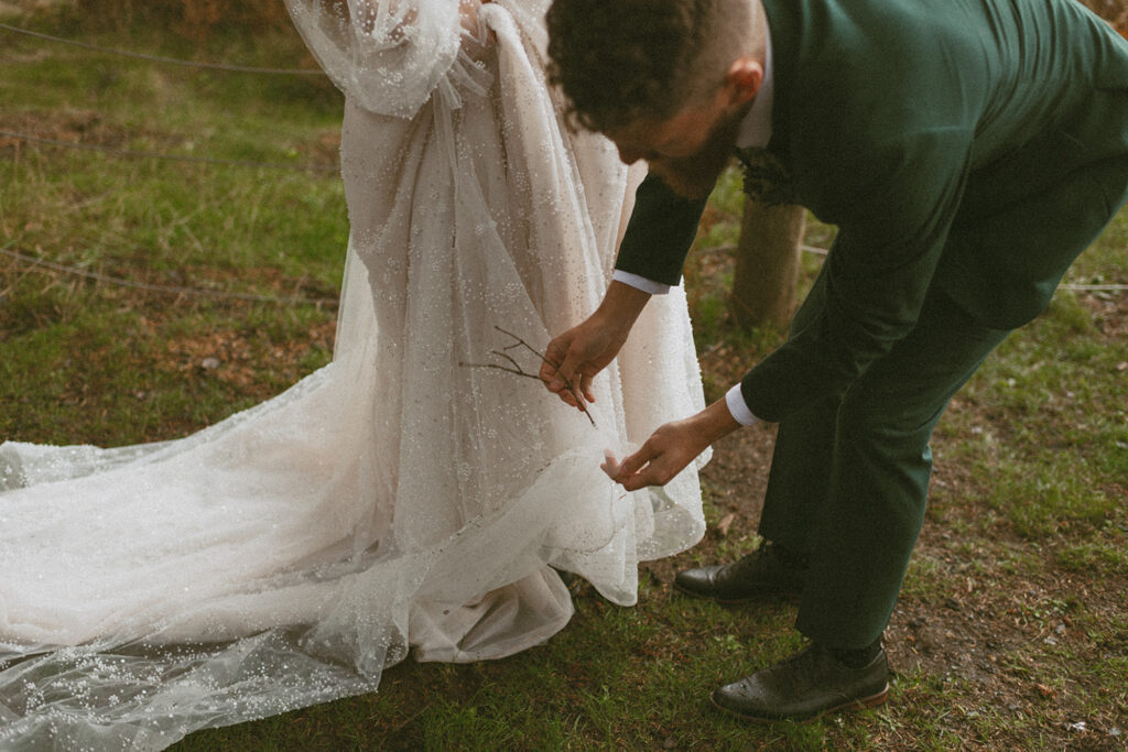 groom removing a twig from a bride's flowy, romantic dress