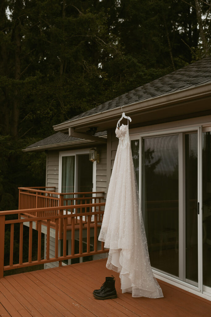white wedding dress hanging on a hanger from the roof of a wooden deck and a pair of black combat boots placed on the deck floor