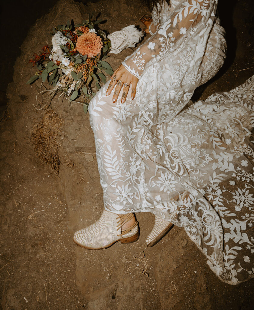 bride in a lace wedding dress, visible from the waist down, wearing white boots holding floral bouquet
